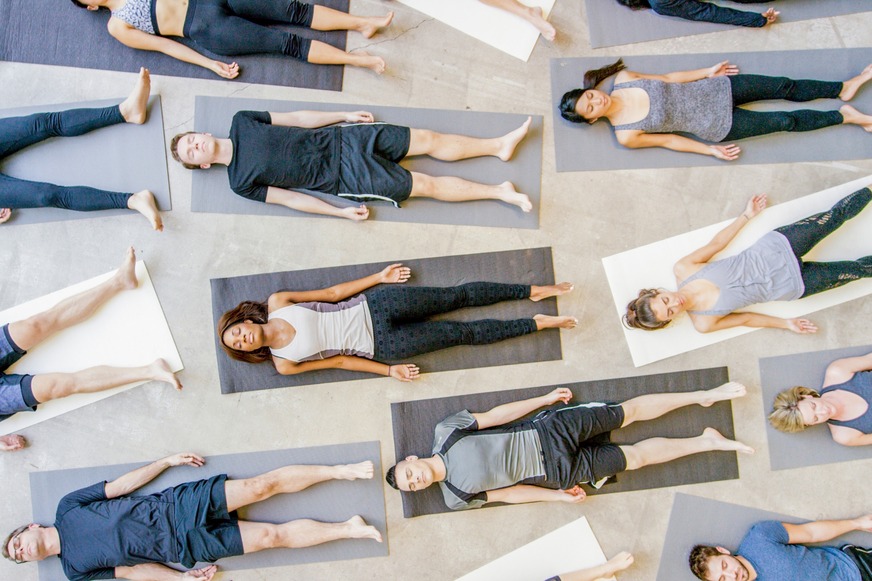 an overhead view of multiple people laying flat on yoga mats on the floor in savasana pose with their eyes closed